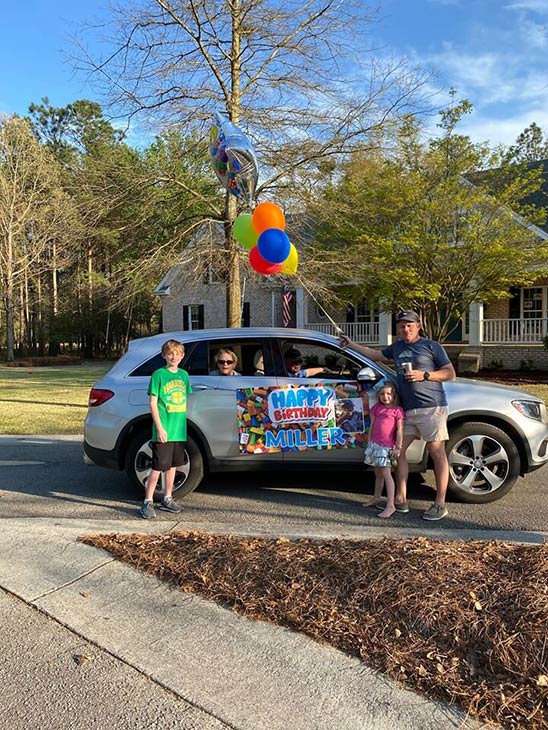 Photo of residents in a car with others people standing around the car